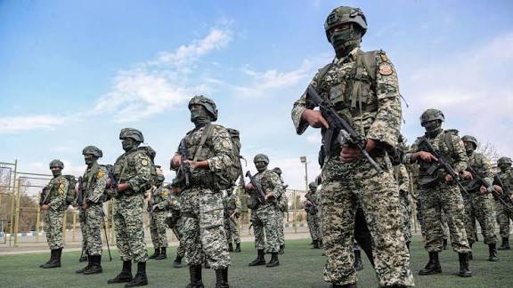 Masked armed men carrying rifles during a protest rally with flags in Iran